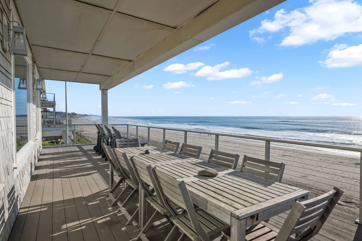 A spacious outdoor deck features a long dining table, a retractable awning, and breathtaking ocean views. The setup is ideal for outdoor dining, lounging, or evening gatherings, capturing the blend of comfort and natural beauty.
