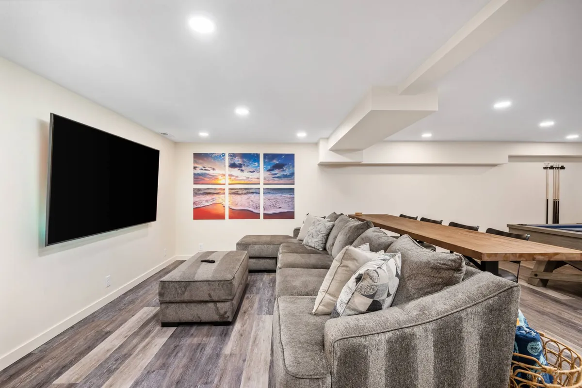 A spacious, inviting interior features a large flat-screen TV, cozy sectional sofa, a dining table perfect for meetings or shared meals, a pool table for recreation, and tasteful wall art. The room receives natural light and offers multiple seating and activity zones ideal for group connection and downtime.
