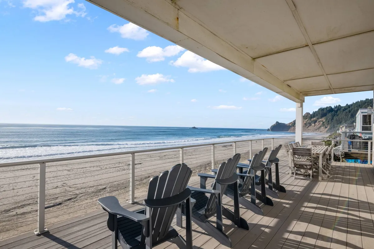 An inviting exterior scene with deck chairs facing the ocean, a sandy beach stretching out, and a serene sky overhead. The set-up suggests opportunities for sunbathing, reading, or enjoying group conversations as waves provide a soothing soundtrack. The view reinforces the home’s proximity to natural beauty and outdoor leisure.