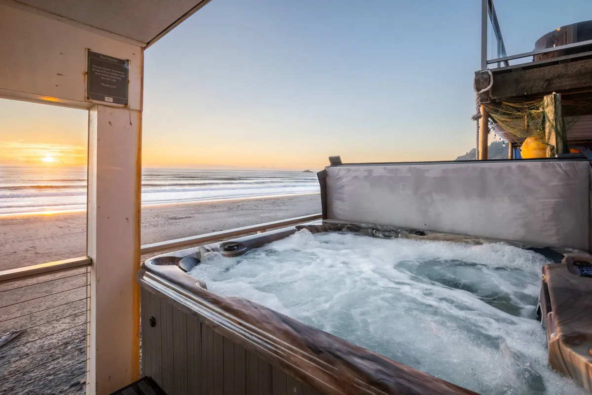 An outdoor hot tub sits on a deck overlooking the ocean at sunset, with inviting seating and tranquil views. The scene captures the relaxation and luxury of soaking while enjoying ocean vistas and the calming sounds of the waves.