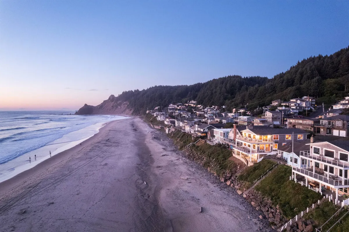 A wide-angle exterior view of the beach, ocean, nearby houses, and a distant mountain. The scene is tranquil and expansive, illustrating the proximity to natural beauty and outdoor adventure. Activities like beachcombing, fishing, and sunset watching are all suggested by the scene.