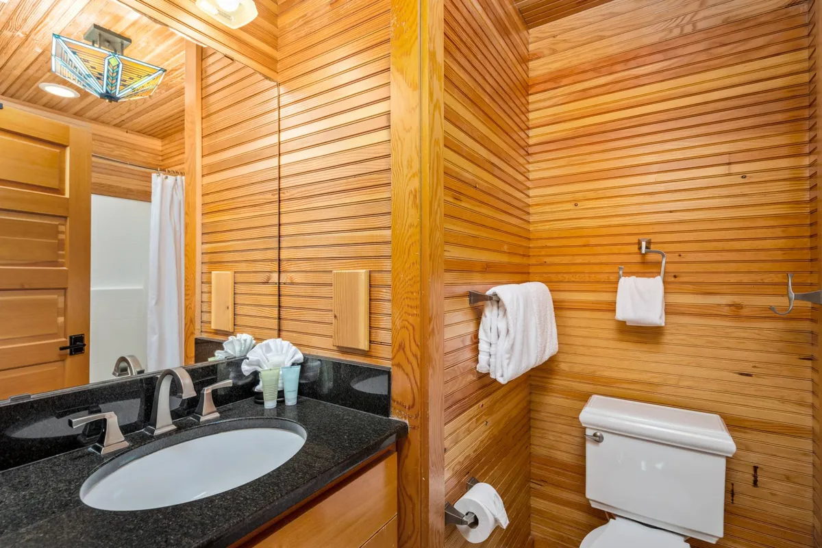 A serene bathroom with granite countertops, wood paneling, a large mirror, and soft lighting. The calm ambiance invites relaxation, suggesting both practical everyday use and moments of peaceful retreat.