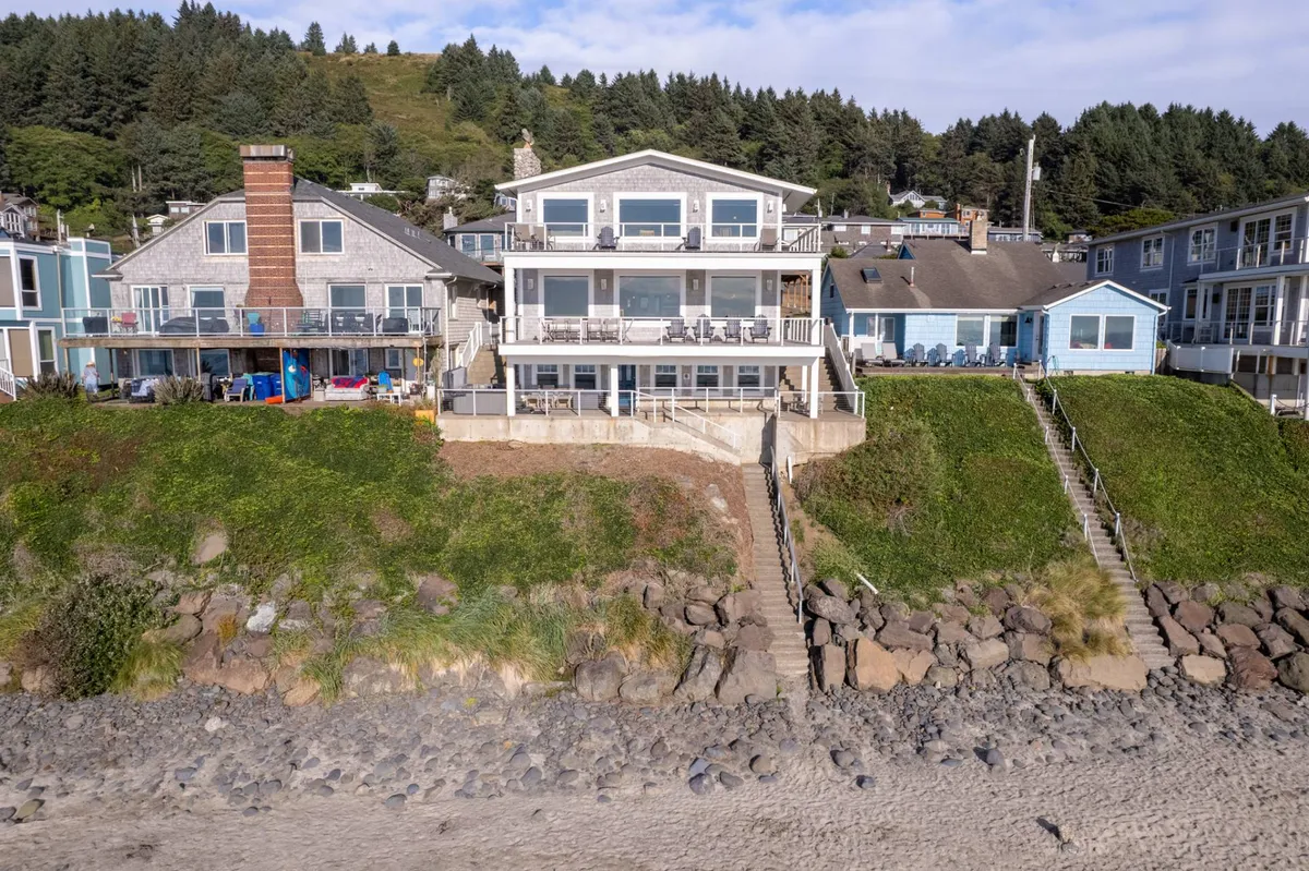 A spacious beachfront property is shown with multiple outdoor seating areas and a staircase leading directly to the sand. The setup encourages beach walks, outdoor dining, and sunbathing, all with the ocean as a backdrop. The scene is lively yet relaxed, well-suited for large groups or families.