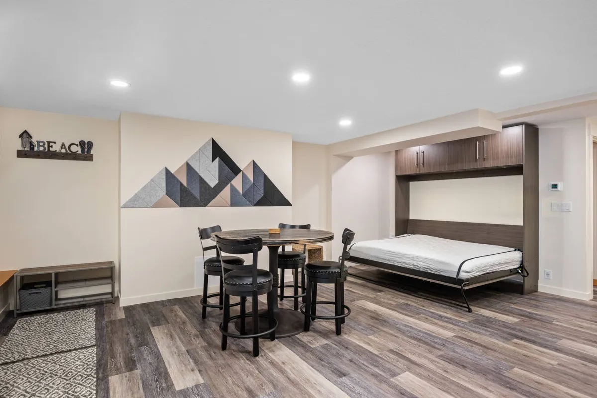 A flexible bonus room featuring stylish wall art, a dining table, and a foldable bed, creating an inviting multipurpose space for relaxing, dining, or transforming into an extra sleeping area when needed.