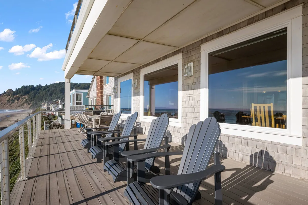 This image captures a wooden deck set with Adirondack chairs facing a sweeping, unobstructed view of the ocean. The arrangement and open space evoke a sense of calm and invite visitors to sit and soak in the horizon, whether for a peaceful morning coffee or group conversation as the waves break below.