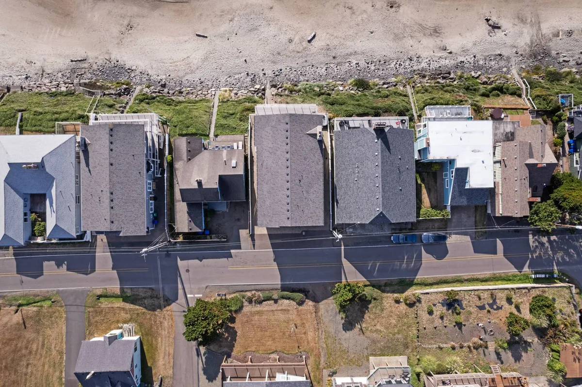 A wide exterior shot showing rows of houses lining the beachfront, with a sandy road and abundant greenery. The beach is visible just steps away, suggesting easy access to outdoor activities and community experiences.