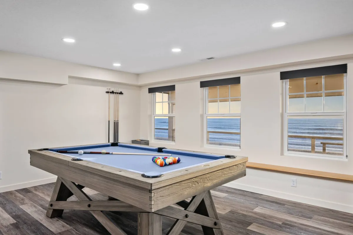 An interior shot of a casual entertainment room with a pool table and large windows that provide a sweeping ocean view. The room is designed for socializing and leisure, making it ideal for games while staying connected to the beautiful coastal scenery.